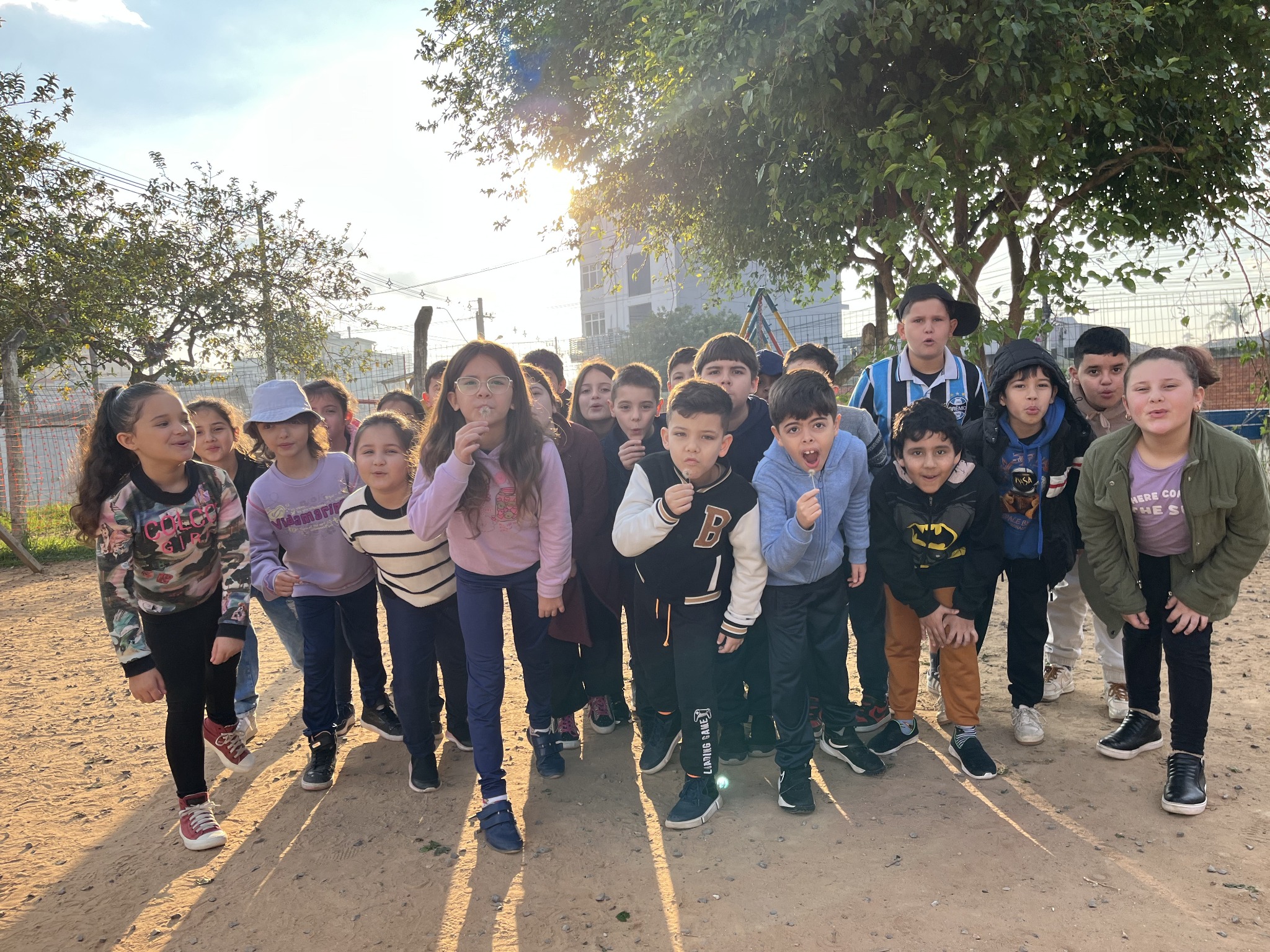 Alunos da Turma 32 reunidos ao ar livre, alguns soprando sementes de dente-de-leão.